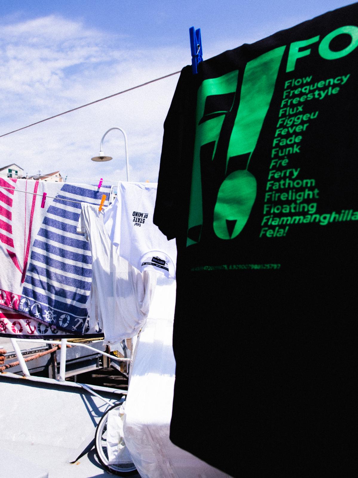F!-Shirt nera con stampa verde esposta in spiaggia